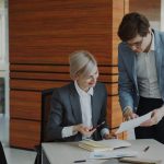 Two colleagues discussing documents at an office desk.
